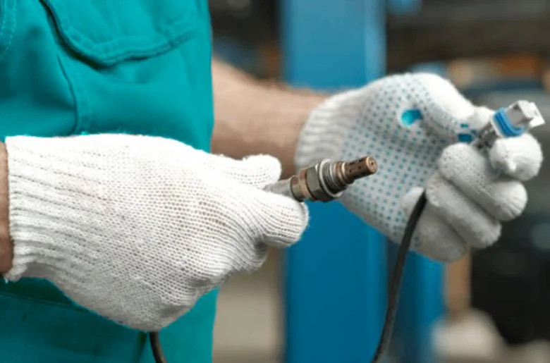 Mechanik drží zapalovací svíčku a senzor kyslíku v dílně.
