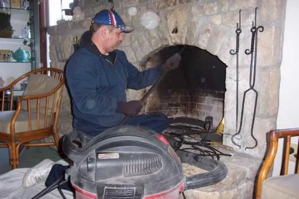 Muž čistí kamneň pomocí nástrojů a vysavače uvnitř domu.