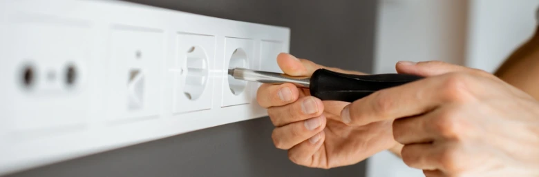 Ruční instalace elektrické zásuvky do zdi pomocí šroubováku.