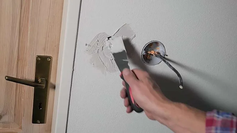 Ruka natíří hmotu kolem otvoru pro elektrickou zásuvku.