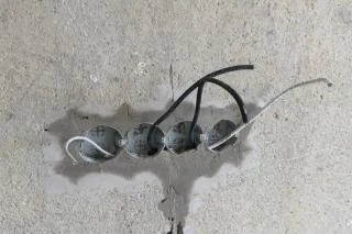 Čtyři elektrické kabely vyvedené z otvoru v betonové stěně panelového domu.