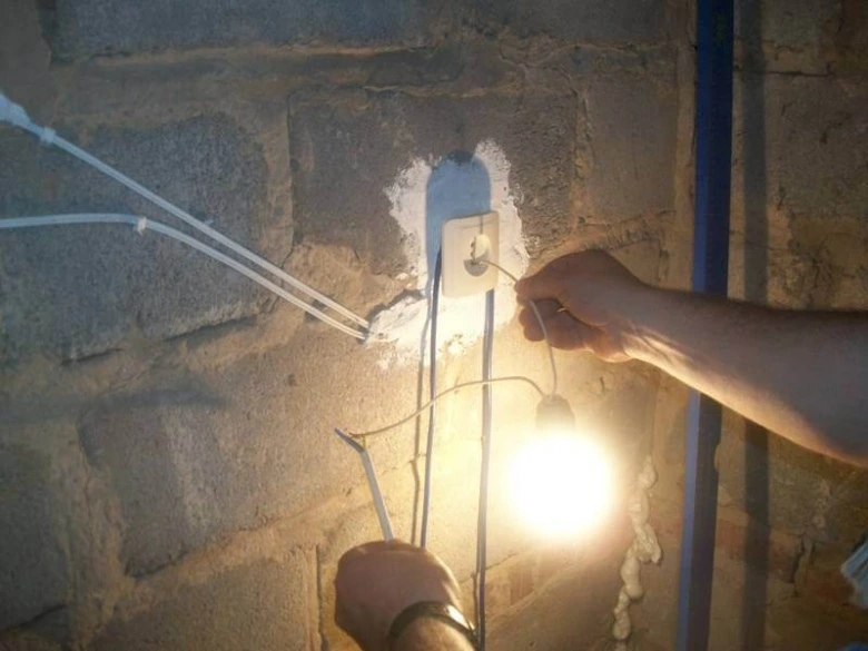 Ruce kontrolují elektrické dráty pomocí žárovky pro ověření napětí.