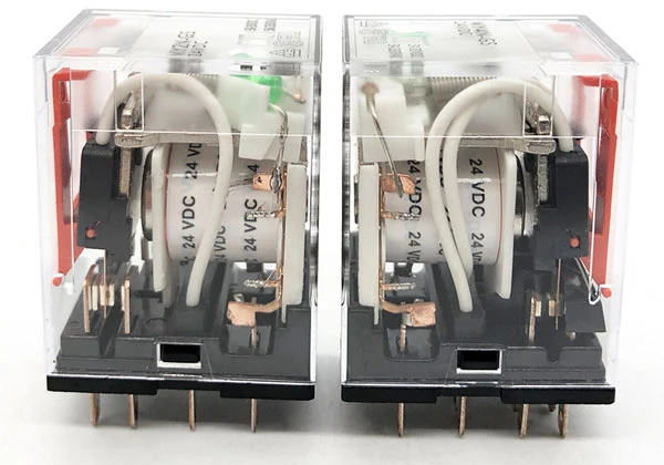 Dva průhledná elektromagnetická relé s viditelnými cívkami a kontakty pro ukázku principu činnosti.