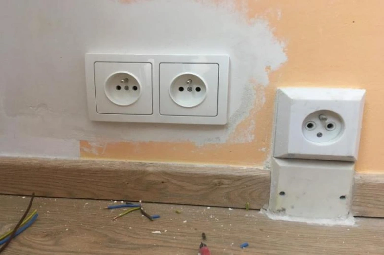 Instalace elektrických zásuvek v panelovém domě s odhalenými vodiči.