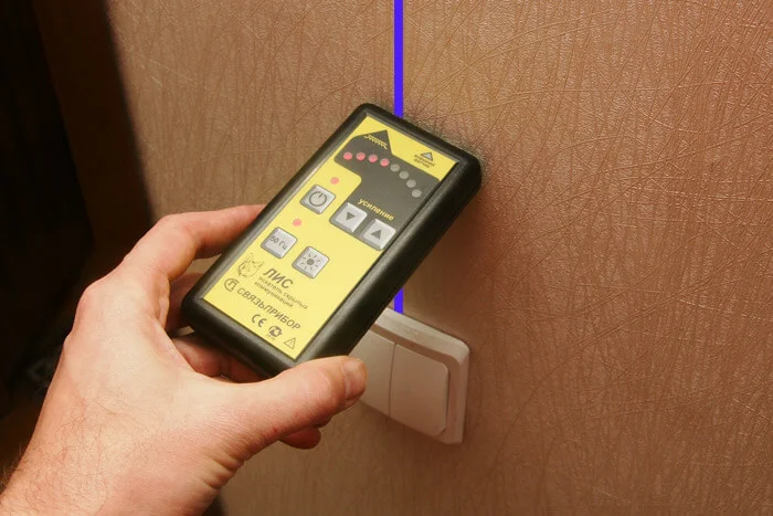 Ruka drží laserový úrovně s modrou čarou na zdi.