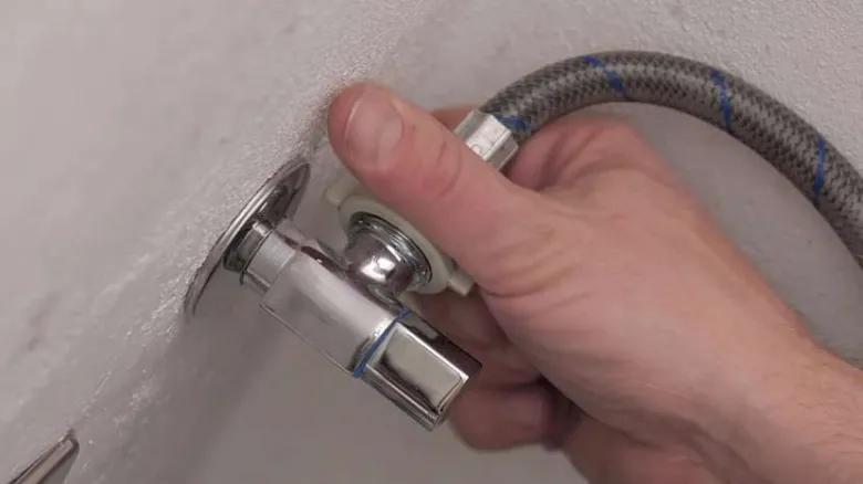 Ruka připojuje hadici k ventilu pro pračku ve zdi.