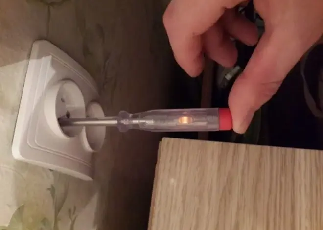 Ruční testér napětí s rozsvícenou lampičkou v elektrické zásuvce.