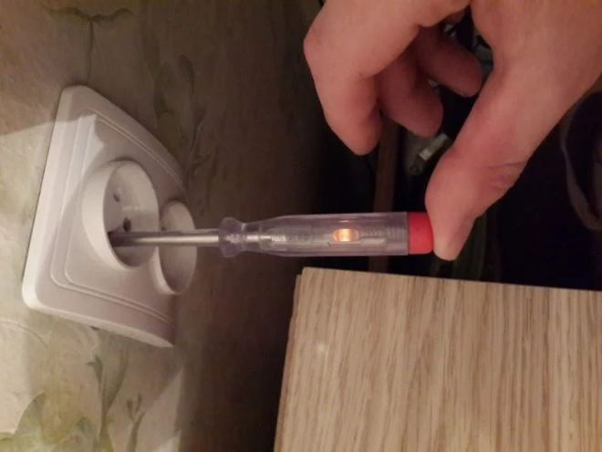 Ruční testér napětí s rozsvícenou lampičkou v elektrické zásuvce.