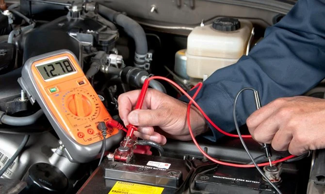 Muž měří napětí automobilové baterie multimetrem pod kapotou.