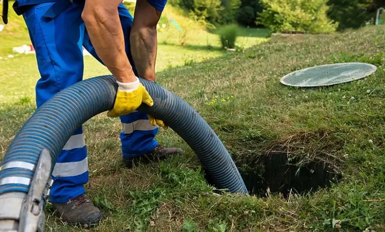 Pracovník čistí septik hadicí u otevřeného poklopu.