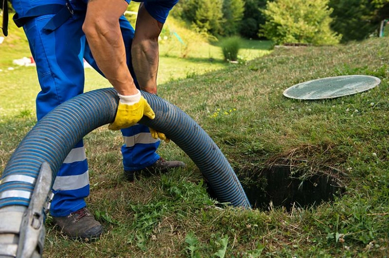 Pracovník čistí septik hadicí u otevřeného poklopu.