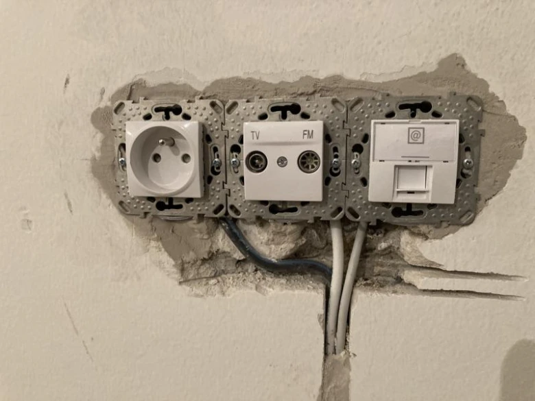 Instalace elektrických zásuvek v panelovém domě s viditelným vedením.