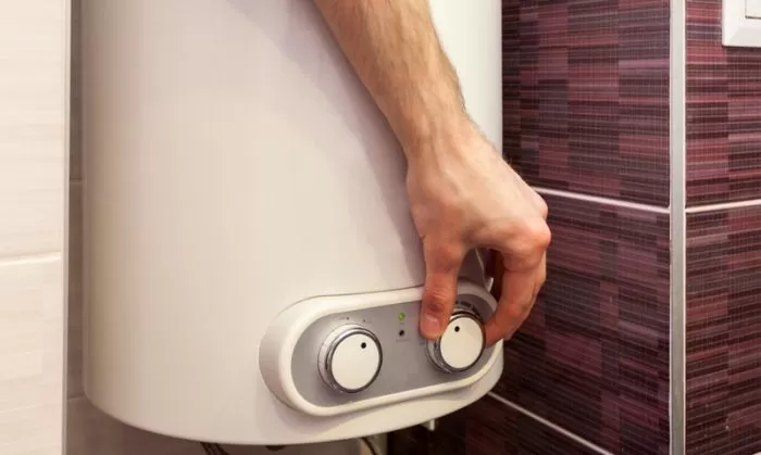 Ruka nastavuje teplotu na elektrickém bojleru pro úsporu energie.