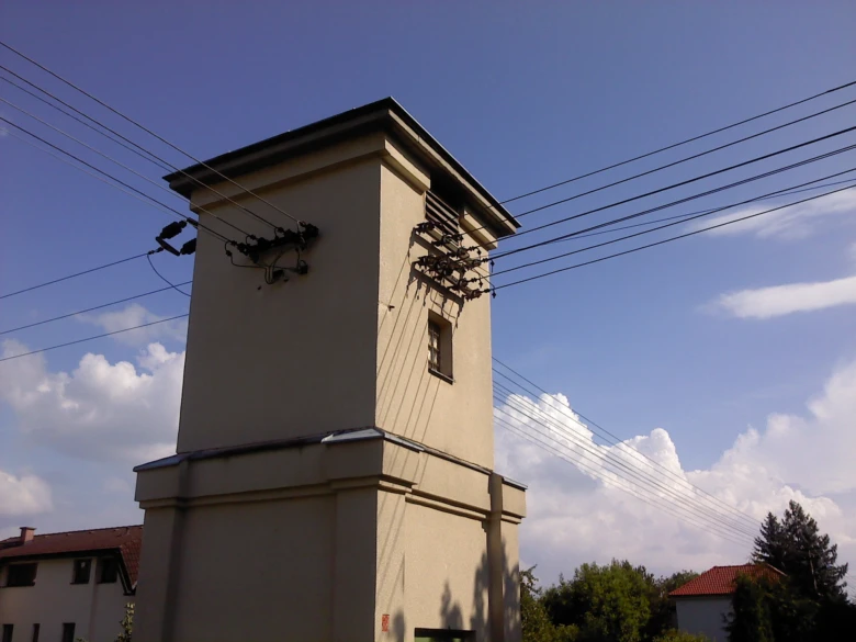 Vysoká rozvodná věž s elektrickými vedeními na modré obloze.
