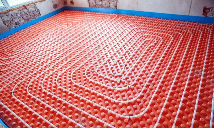 Bílá potrubí pro podlahové topení na oranžovém izolačním panelu.