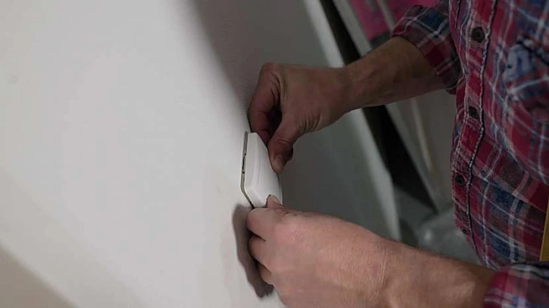 Ruce člověka v křídové košili montují elektrický prodlužovač na zeď.