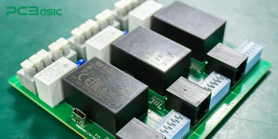 Zelená deska s mnoha elektromagnetickými relémi pro zapojení v elektrotechnice.