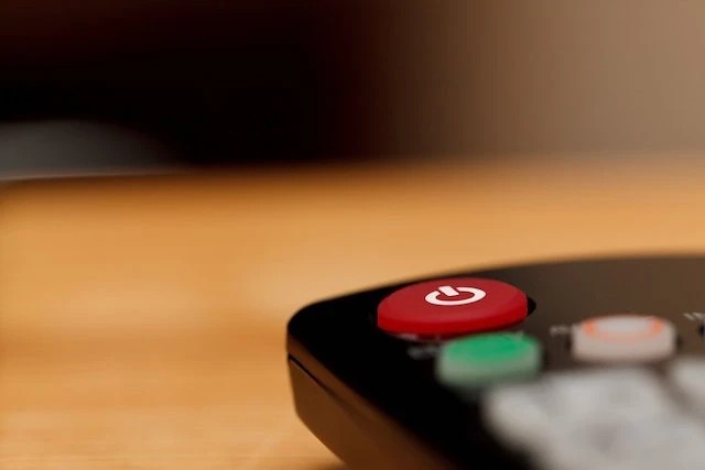 Černý dálkový ovladač s červeným tlačítkem pro zapnutí televize.