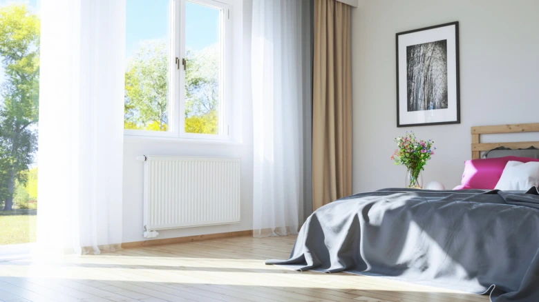 Loft s bílým radiátorem u okna v jasně osvětlené místnosti.