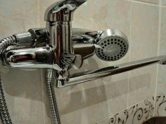 Lesklá sprchová baterie s ruční sprchou namontovaná na dlažbě.