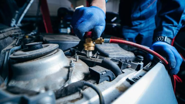 Mechanik doplňuje klimatizaci auta pomocí manometru pod kapotou.