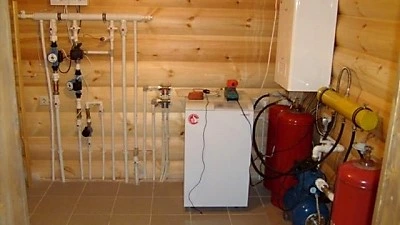 Fotografie topného systému s nádržími a potrubím v technické místnosti.