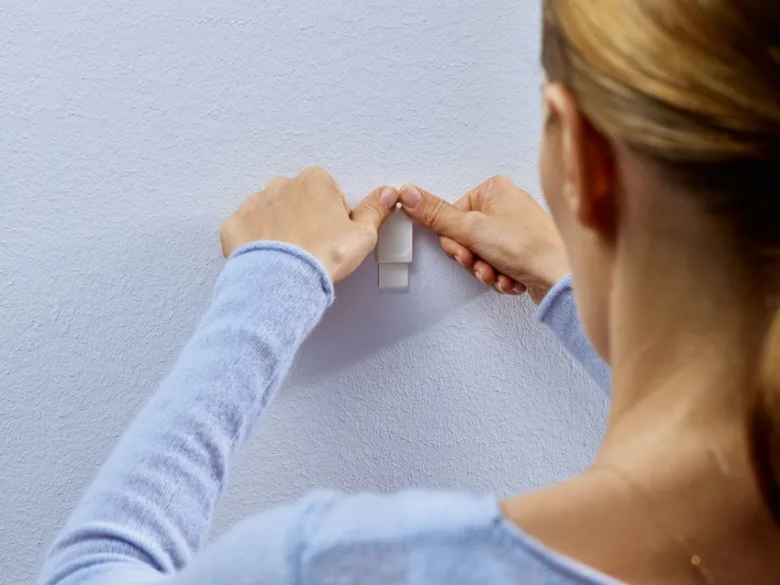 Žena upevňuje bílý držák na stěnu bez vrtání