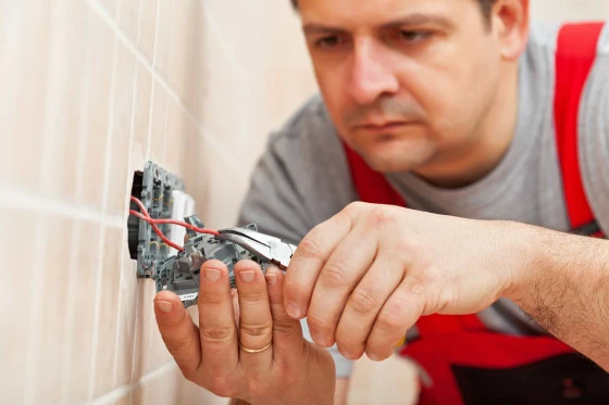 Elektrikář připojuje dráty k nové zásuvce ve zdi.