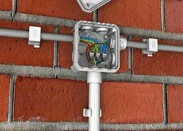 Otevřená elektrická spojovací krabice s připojenými vodiči na cihlové zdi.