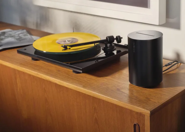 Černý gramofon s žlutou desitou vedle reproduktoru na dřevěném nábytku.