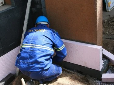 Montážní dělník ukládá izolační desky podél základu zdi.