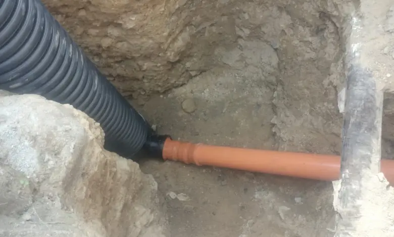 Černá žebrová kanalizační trubka připojená k oranžové v jámě.
