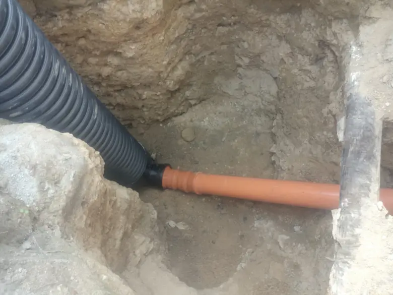 Černé oranžové plastové kanalizační trubice v zemi při instalaci