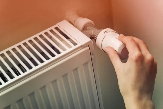 Ruka zavírá termostat na radiátoru před zimou.
