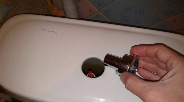 Ruka drží vyjmutý ventil pro toaletní nádrž s otevřeným otvorem.