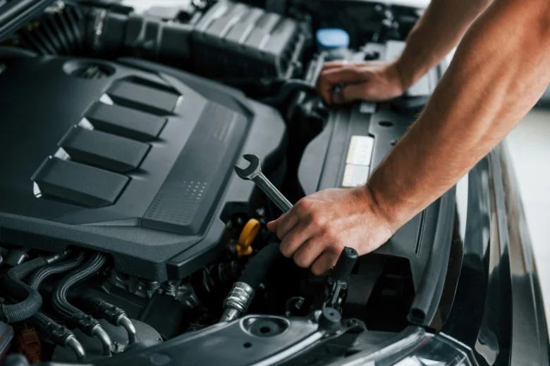 Mechanik opravuje motor automobilu pomocí klíče.