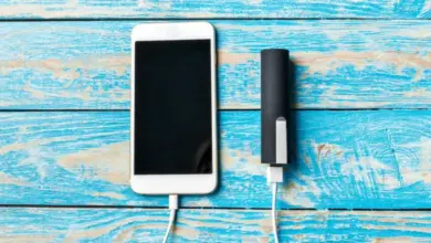 Bílý chytrý telefon nabíjený externím akumulátorem na modrém dřevěném povrchu.