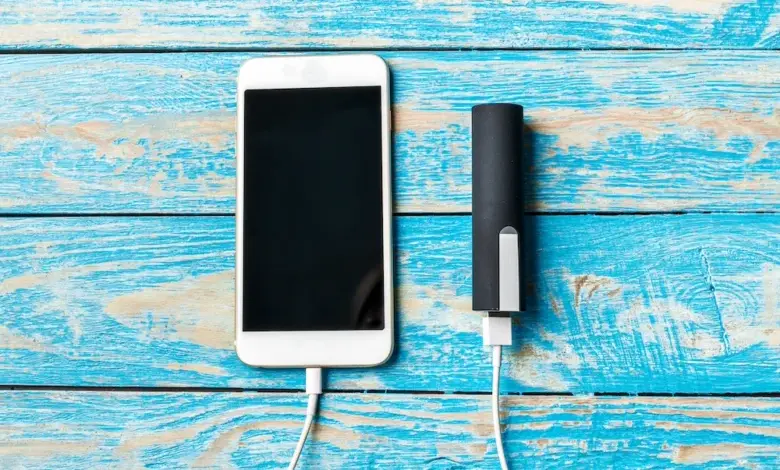 Bílý chytrý telefon nabíjený externím akumulátorem na modrém dřevěném povrchu.