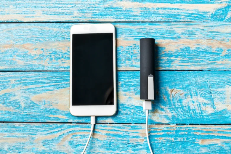 Bílý chytrý telefon nabíjený externím akumulátorem na modrém dřevěném povrchu.