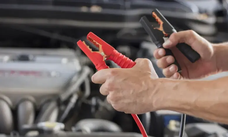 Ruční připojení nabíjecích kabelů k automobilové baterii pod kapotou.