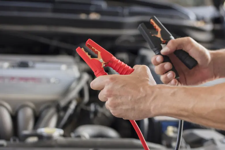Ruční připojení nabíjecích kabelů k automobilové baterii pod kapotou.