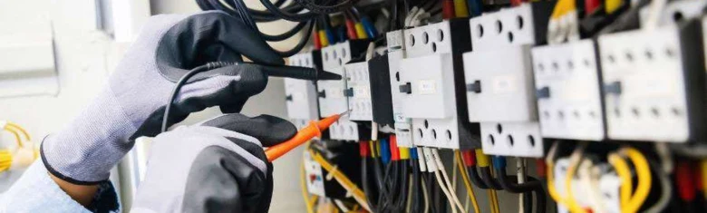 Elektrikář měří napětí na třífázovém jističi v rozvaděči.
