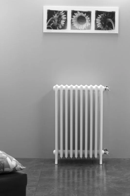 Bílý ocelový radiátor v interiéru s obrazem slunečnic nad ním.