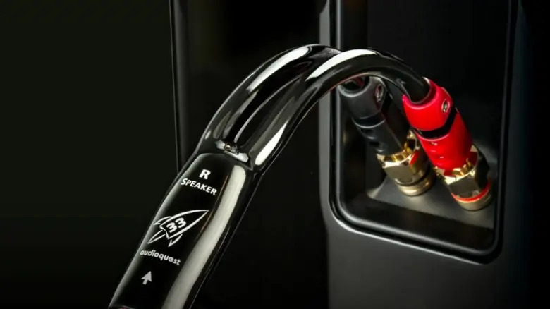 Černý kabel pro reproduktor připojený k zesilovači s červenými svorkami.