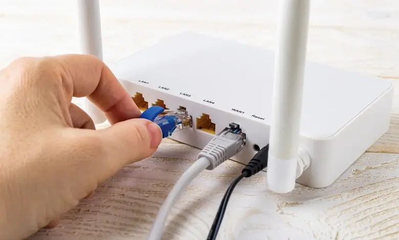 Ruka zapojuje síťový kabel do portu na bílém Wi-Fi routru.
