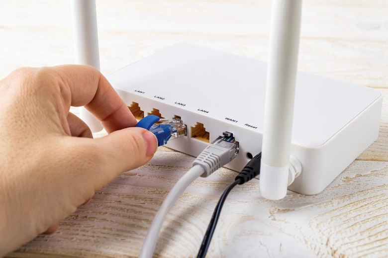 Ruka zapojuje síťový kabel do portu na bílém Wi-Fi routru.