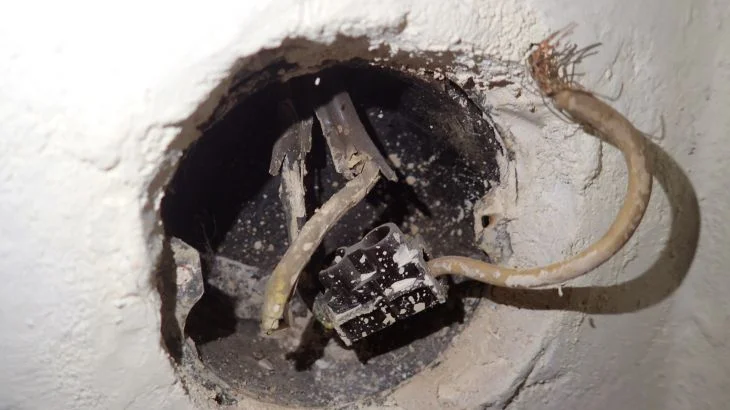 Poškozené elektrické zásuvky s viditelnými vodiči v zdi.