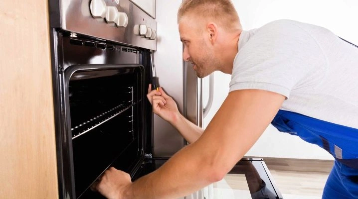 Muž opravuje elektrický sporák šroubovákem u otevřené trouby.