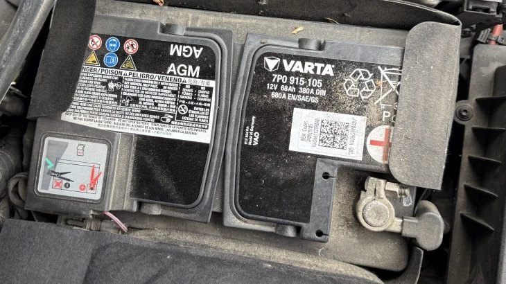 Pohled na automobilovou baterii s viditelnými póly a varovnými štítky.