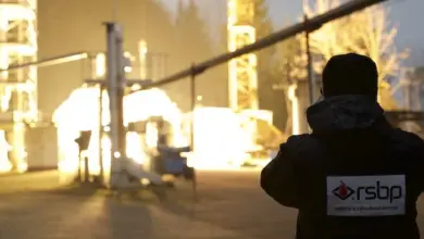 Osoba v ochranném oděvu u průmyslového zařízení s propanovými nádržemi.